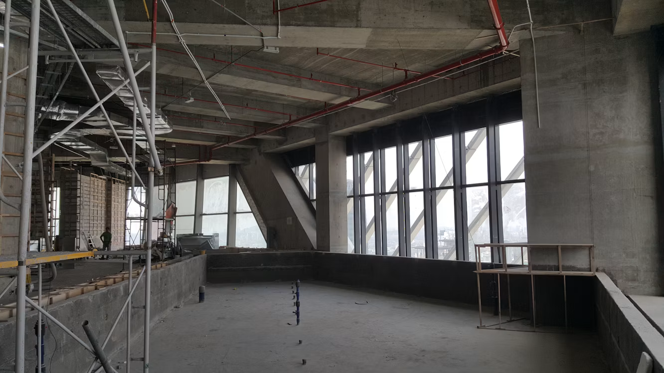 Interior de um edifício em obra, com estrutura de concreto, andaimes e grandes janelas